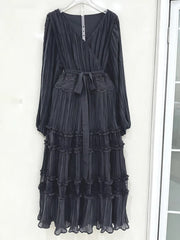 Black pleated dress with lace details on a hanger against a white wall.
