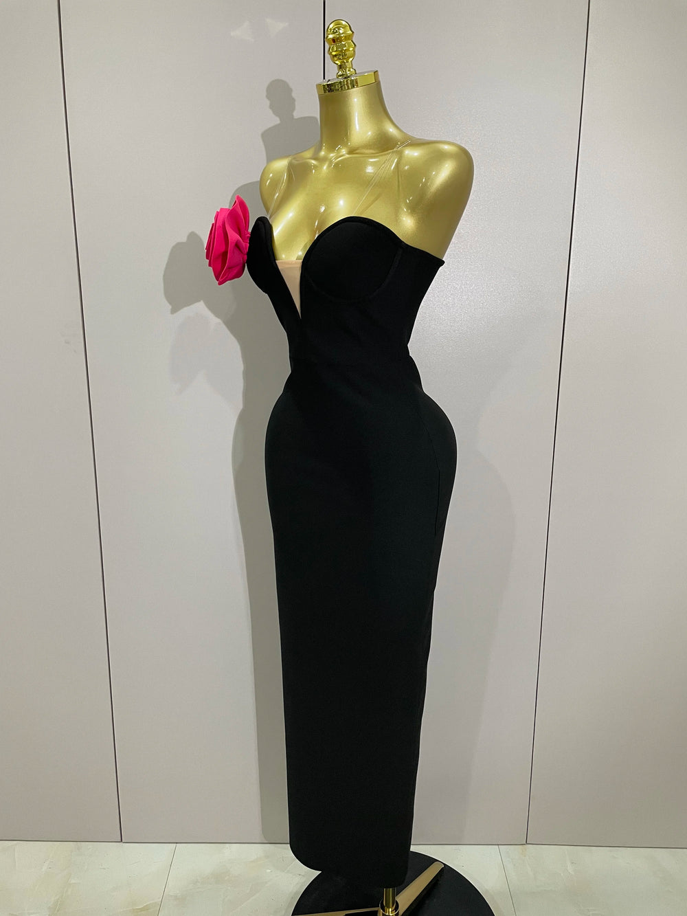 Black evening gown on a gold mannequin with a pink flower against a white background