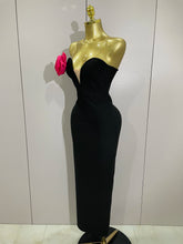 Black evening gown on a gold mannequin with a pink flower against a white background