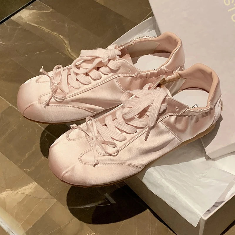 Pink satin ballet sneakers with round toe and lace-up closure.
