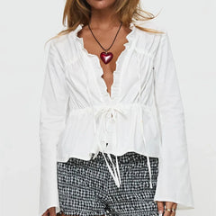 Woman wearing a white blouse with a deep neckline and plaid pants on a plain background