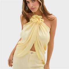 Yellow halter crop top with ruffled flower detail and draped asymmetric hem.