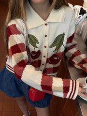 Person wearing a red and white patterned cardigan with a cherry design, holding a cup.