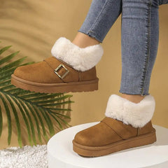 Brown suede boots with white fur trim worn by a person in jeans against a beige background.
