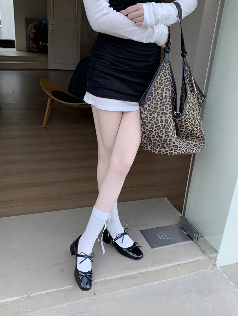 Person wearing a black skirt, white shirt, and black shoes with a leopard print bag.