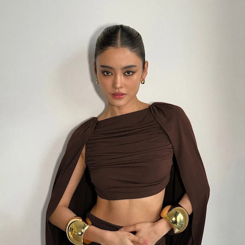 Woman wearing a brown outfit with gold accessories against a plain background