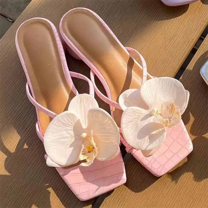 Pink sandals with white orchids on a wooden surface