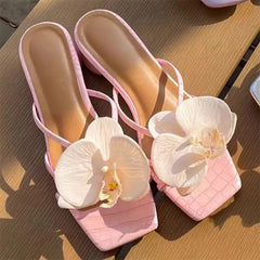 Pink sandals with white orchids on a wooden surface