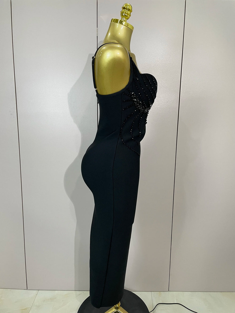 Black evening gown with beaded details on a mannequin against a plain background
