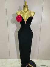 Black evening gown on a mannequin with a pink flower against a white wall