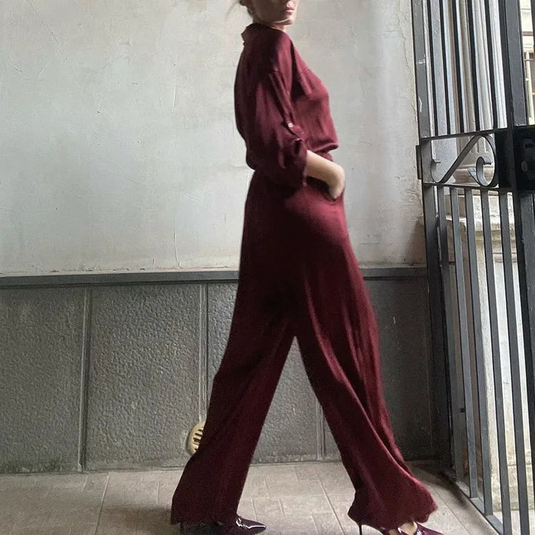 Person wearing a burgundy outfit standing against a neutral wall.