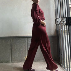Person wearing a burgundy outfit standing against a neutral wall.