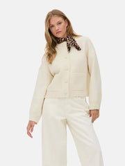 Woman wearing a cream cardigan and pants with a leopard print scarf on a white background