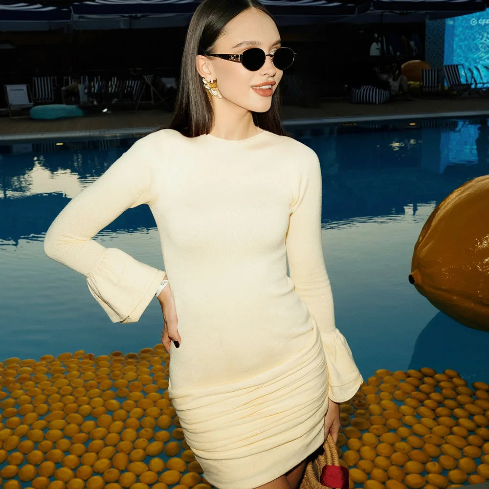 Woman in a cream dress standing by a pool with pool toys in the foreground