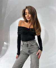 Woman wearing a black off-shoulder top and gray jeans against a light gray background
