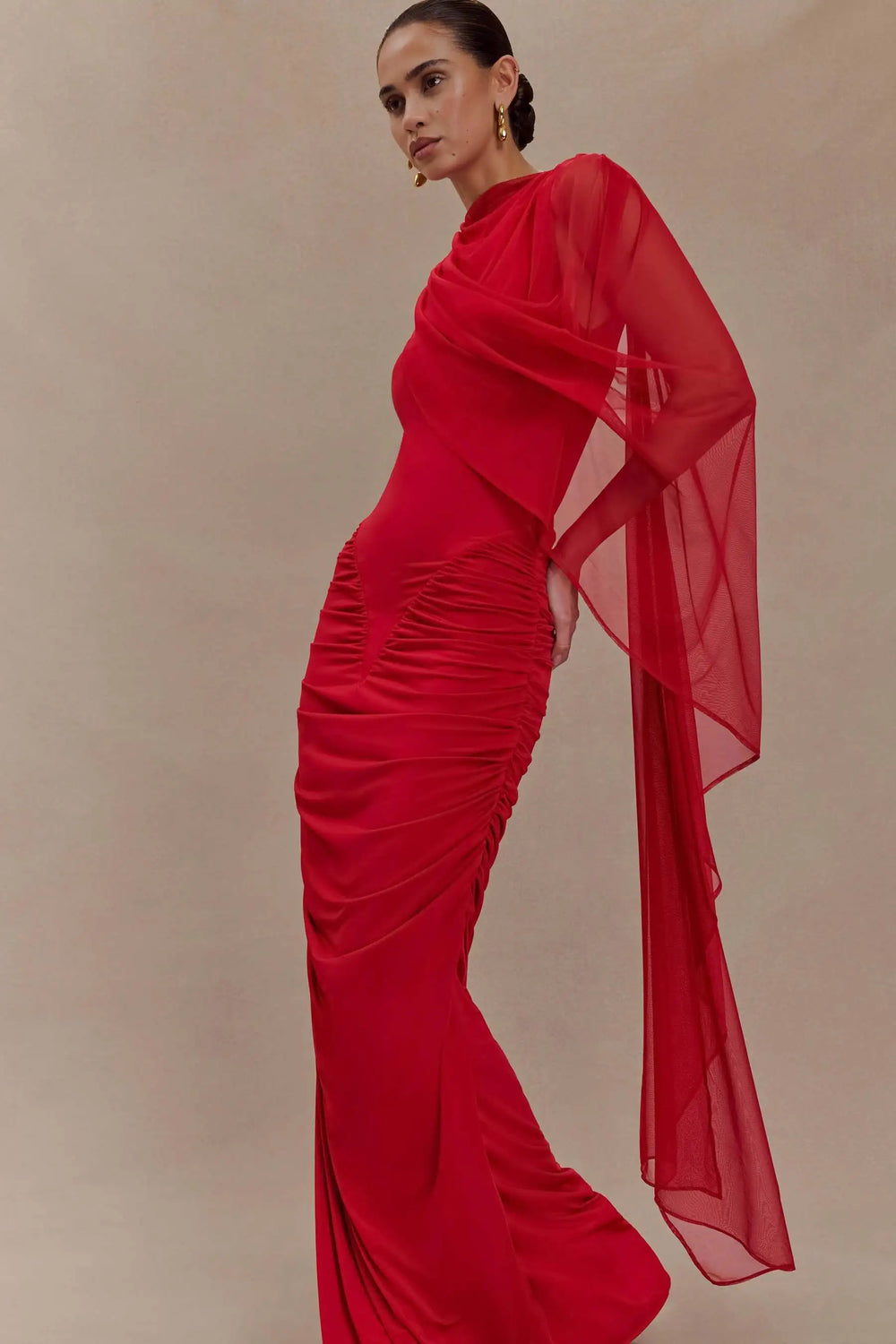 Woman wearing a red evening gown with a sheer overlay against a beige background