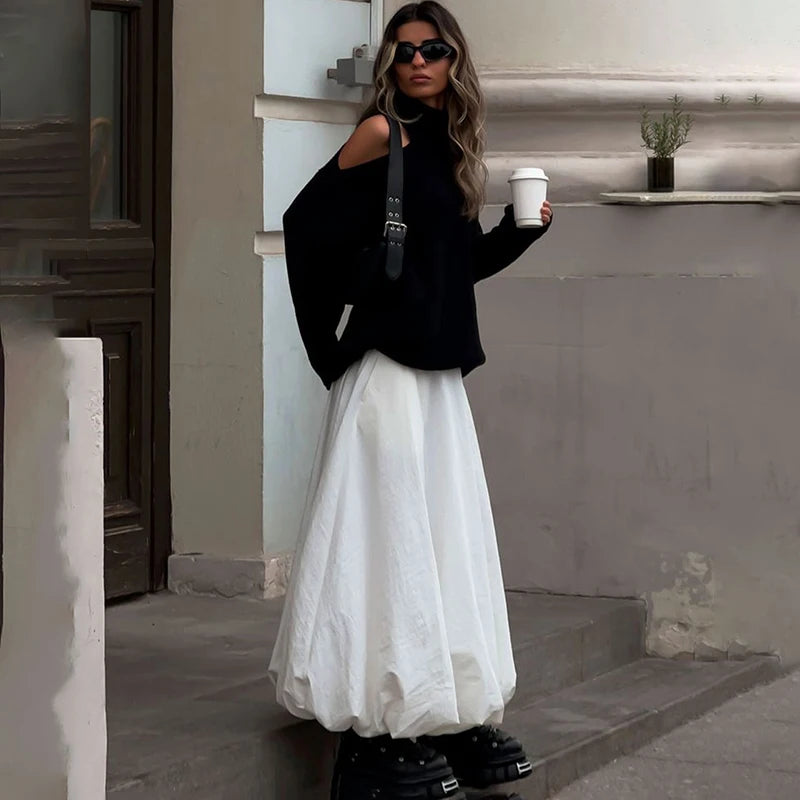 Woman in black top and white skirt holding a coffee cup outdoors.