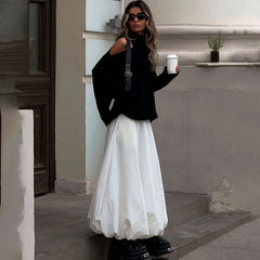 Woman in black top and white skirt holding a coffee cup outdoors.