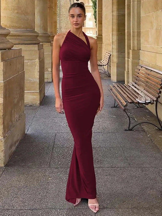 Woman in a burgundy evening gown standing outdoors near stone columns and a bench.