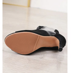 Black ankle boot with brown sole on a light wooden floor