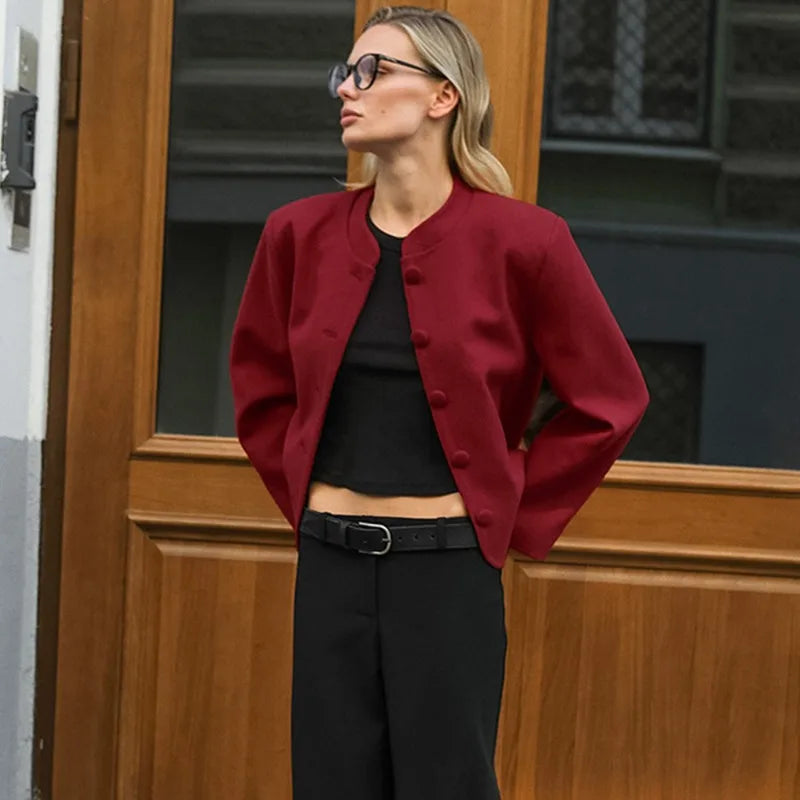 Woman wearing a red jacket and black outfit standing in front of a wooden door.