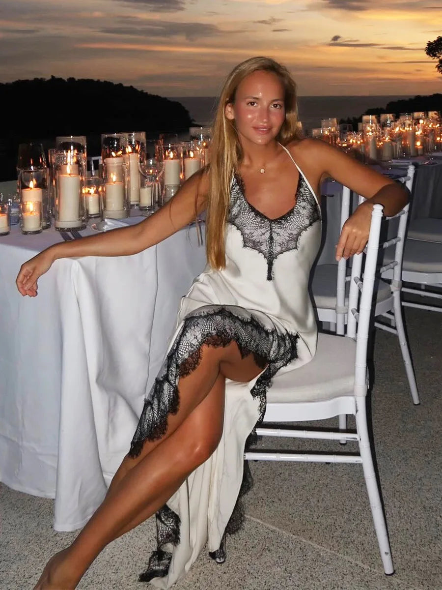 Woman in a black and white dress sitting at an outdoor event with candles and a scenic background.