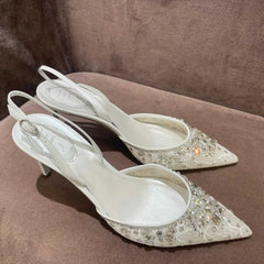 Pair of white high-heeled shoes with crystal embellishments on a brown surface
