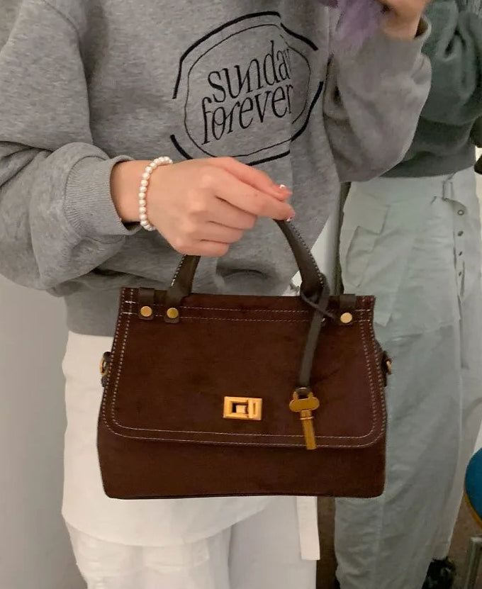 Person holding a brown handbag with a gray sweatshirt and light pants in the background