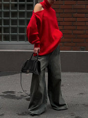 Person wearing a red sweater and gray pants holding a black handbag against a brick wall.