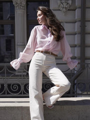 Woman wearing a pink blouse and white pants standing in front of an architectural building.