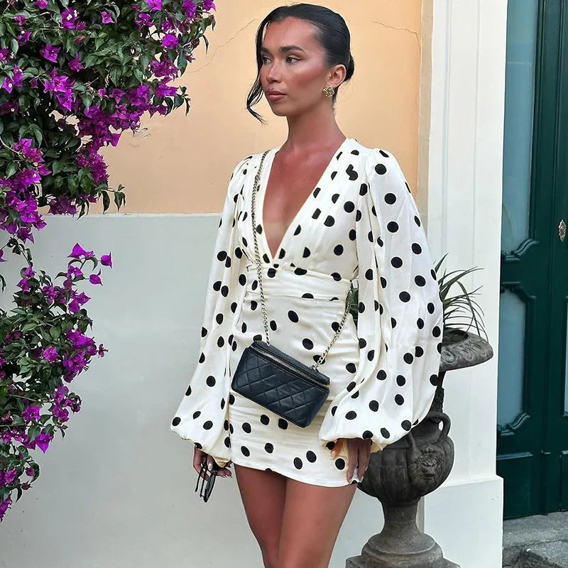 Woman in a polka dot dress standing outdoors with flowers and a building in the background