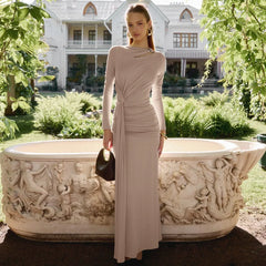 Woman in a beige dress standing next to an ornate stone bathtub in a garden setting.