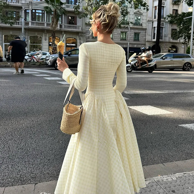 Woman in a long yellow dress standing on a city street, holding an ice cream cone.