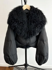 Black cropped puffer jacket with a large black curly textured fur collar and full sleeves.