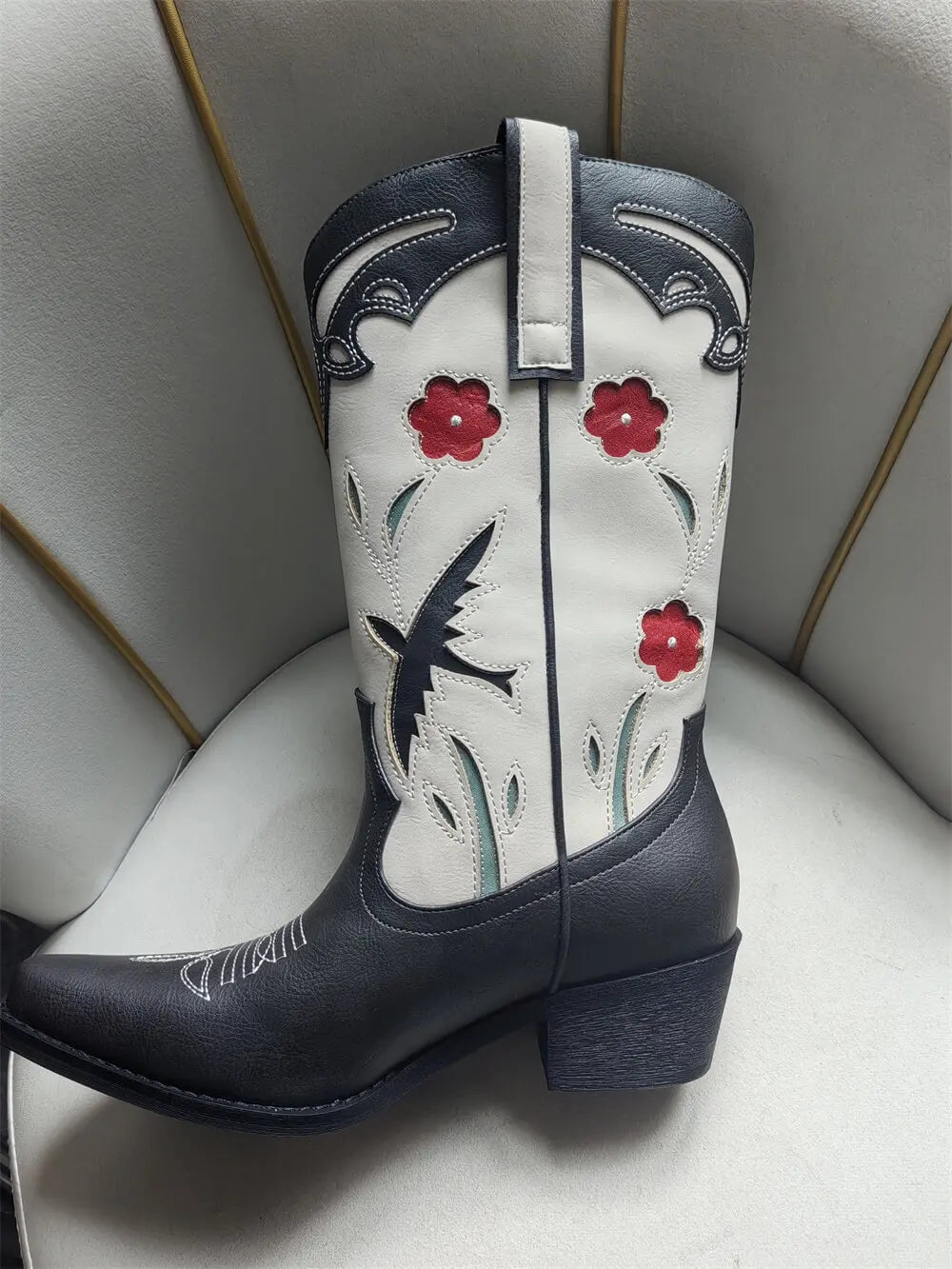 White cowboy boot with black accents and red flowers on a light gray background