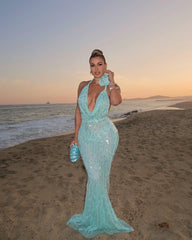 Woman in a light blue evening gown standing on a beach at sunset.