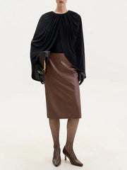 Person wearing a black draped top and brown leather skirt