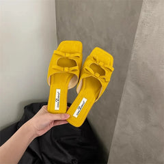 Yellow slippers with a bow held by a hand against a neutral background