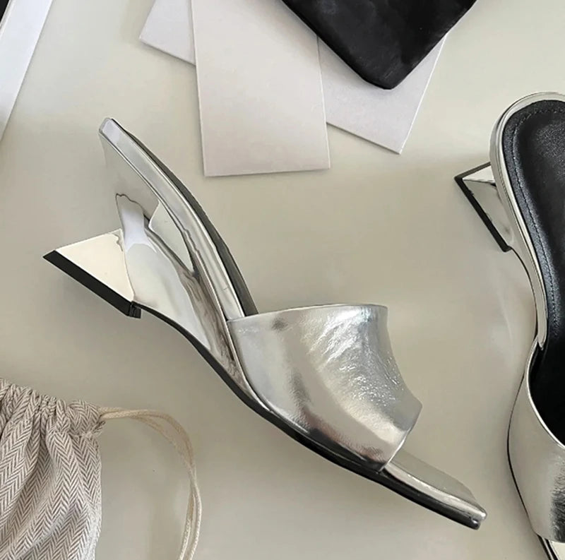 Silver high-heeled shoes on a light surface with a black bag in the background.