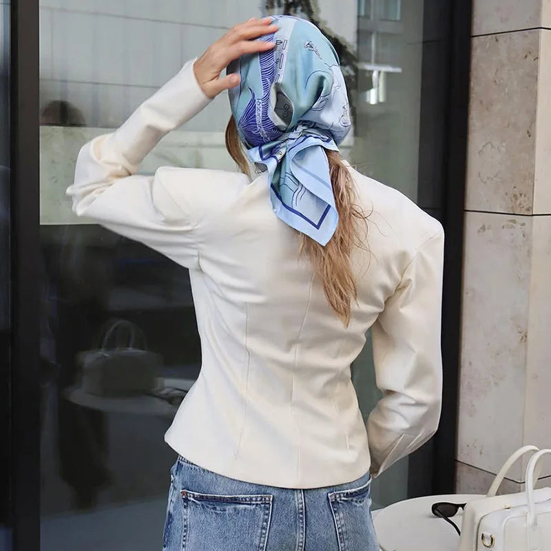 Person wearing a white jacket and blue jeans, adjusting a patterned scarf on their head.