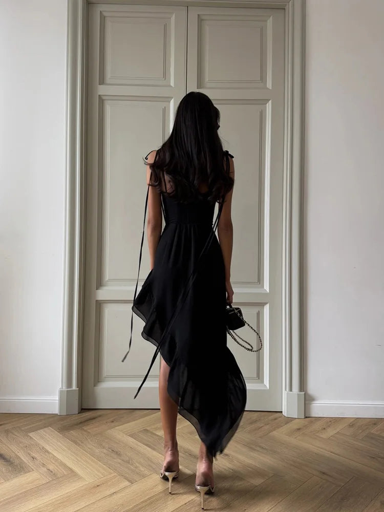 Woman in a black dress standing in a room with white walls and wooden floor.