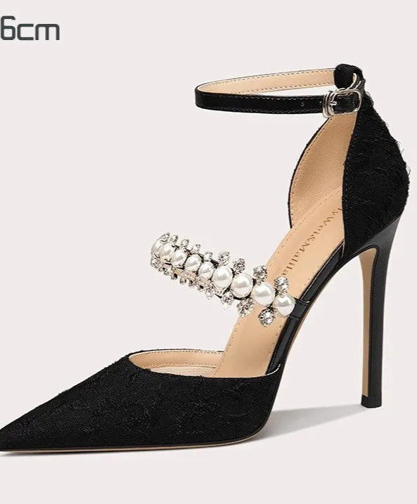 Black high-heeled shoe with pearl embellishments on a light gray background