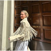 Woman wearing a white fringed jacket standing in front of a wooden door.