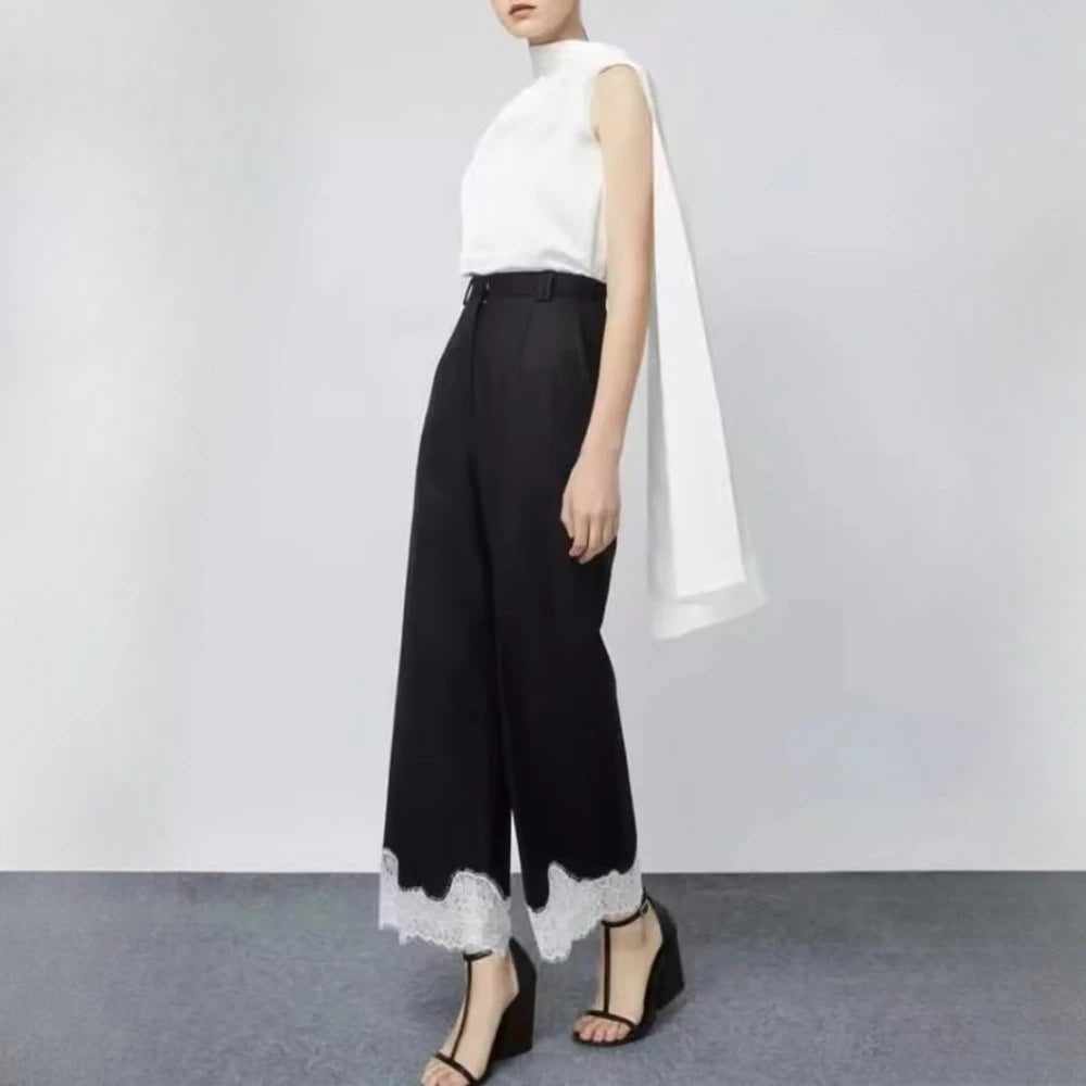 Person wearing a white top and black pants with lace trim on a plain background