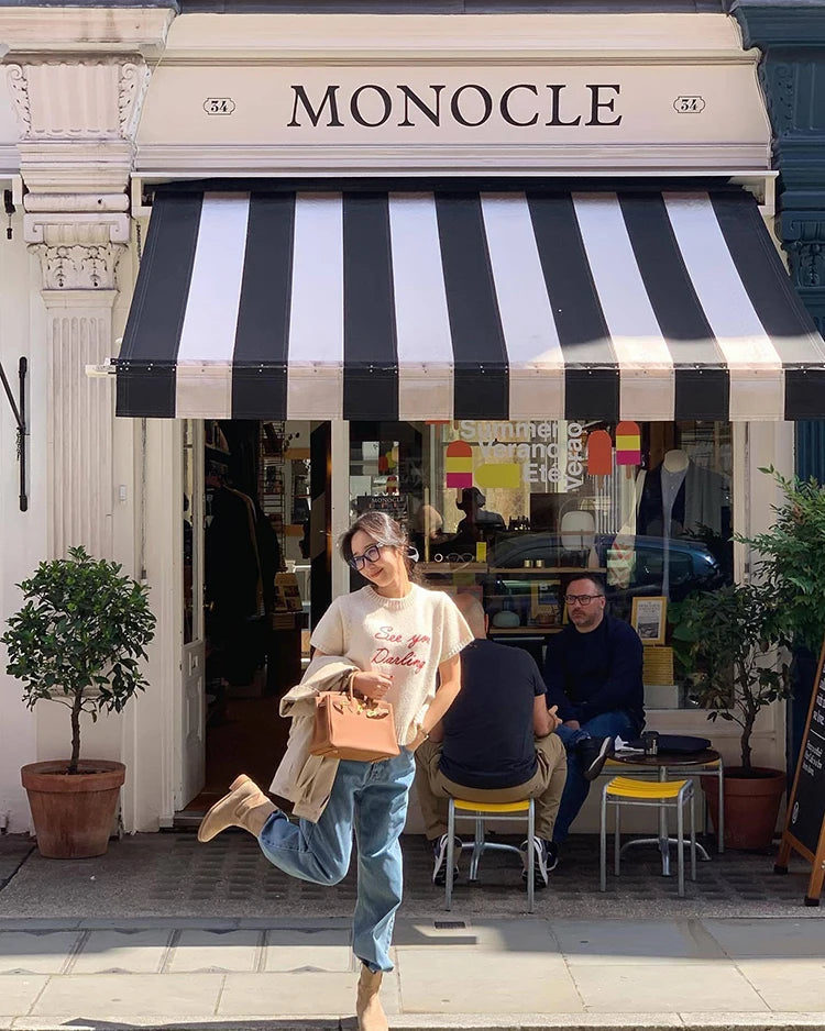 Person standing in front of a store with a striped awning labeled 'Monocle'.