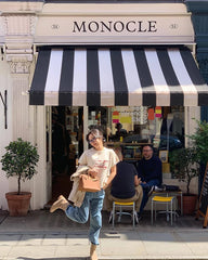 Person standing in front of a store with a striped awning labeled 'Monocle'.