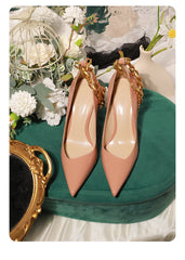 Pair of pink high heels with gold chains on a decorative surface with flowers and a mirror.
