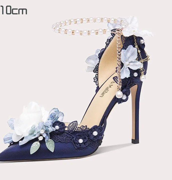 Navy blue high-heeled shoe with floral and pearl details on a white background