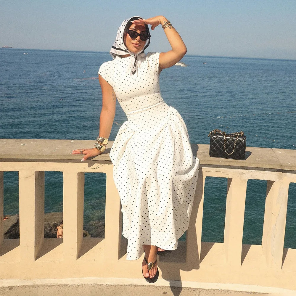 Woman in a white polka dot dress with a headscarf by the sea