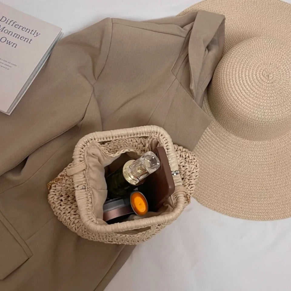 Woven handbag with sunglasses and a book on a beige garment with a straw hat.